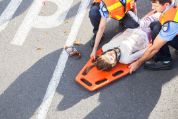 Zwei Sanitäter versorgen am Hals verletzte Frau auf orangem Plaste-Tragbrett Zwei Sanitäter versorgen am Hals verletzte Frau auf orangem Plaste-Tragbrett